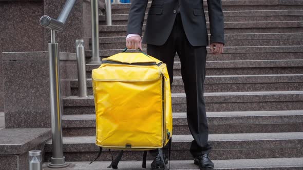 Unrecognizable Man in Formal Suit Standing with Yellow Thermal Backpack on Urban Stairs Outdoors