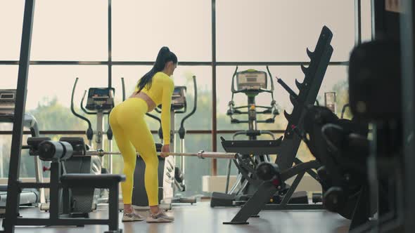 Fit Hispanic Woman Performing Weight Lifting Deadlift Exercise with Barbell at Gym In Yellow