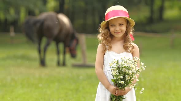 Little Girl Is Standing in a Park with a Bouquet of Wildflowers. Slow Motion