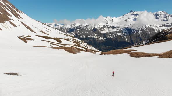 Aerial: flying over hiker walking towards snowy mountain top, ski touring mountaineering snow