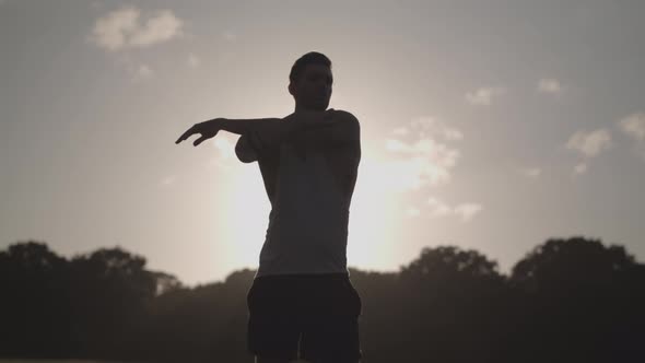 Young Attract Man Stretches In Park Before He Goes For A Run With The Evening Sun In The Background