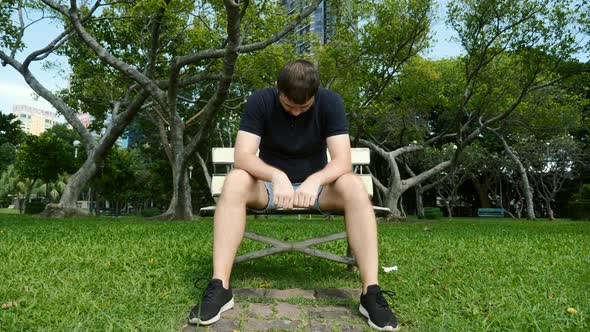 Sad Unhappy Man Sitting Alone on Bench in Park Head Bowed Depressed Worried