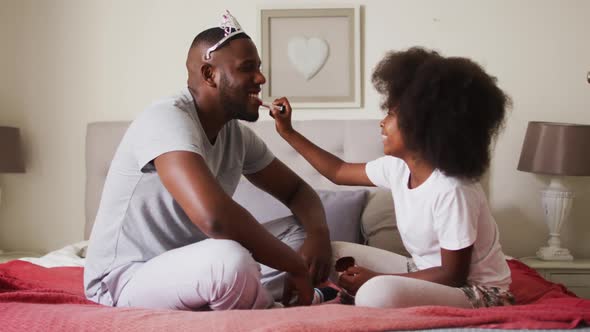 African american girl applying lipstick to her father father wearing crown at home