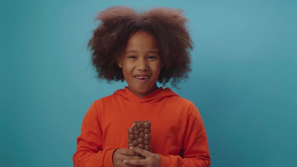 Happy black girl eating chocolate bar holding in hands smiling at camera