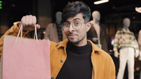 Stylish Joyful Young Guy Shopper Stands in Boutique Points to Packages Satisfied with Good Purchase