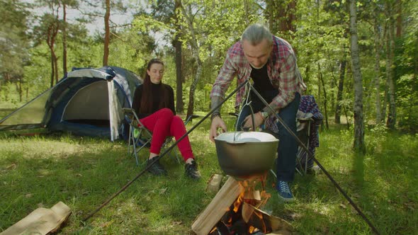 Mature Camper Man Putting Firewood in Campfire During Cooking