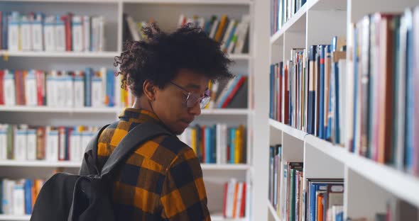 Back View of Young Happy African Student Looking Around in Modern Library