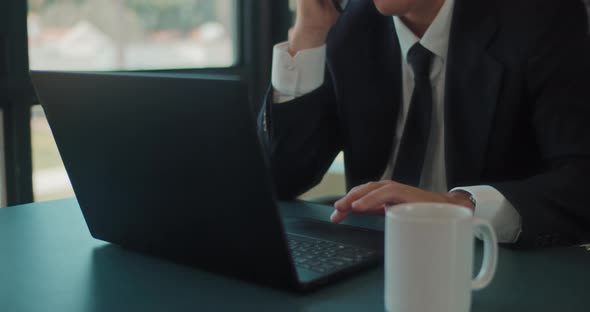 Close up of a businessman working on a laptop while holding a phone. Tracking shot, slow motion. 