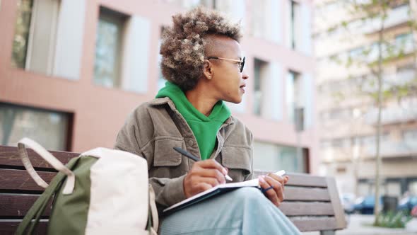 Pensive African woman wearing green hoodie writing notes in notepad