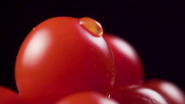 Macro shot of falling water drops in slow motion on ripe cherry tomato. Black backgroun