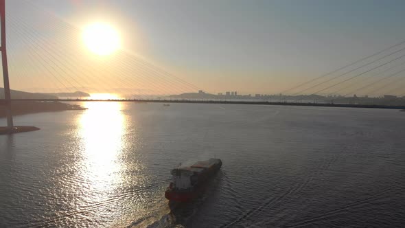 Aerial Shot of a Large Container Ship Moving Into Port Through the Strait with a Big Cable Bridge