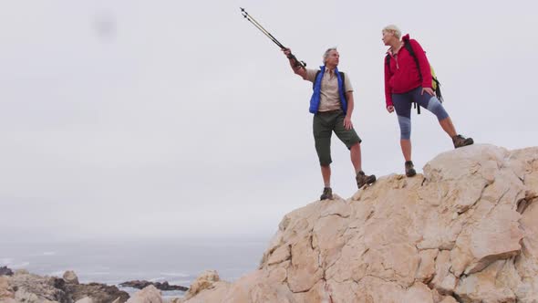 Senior hiker couple with backpack and trekking poles pointing