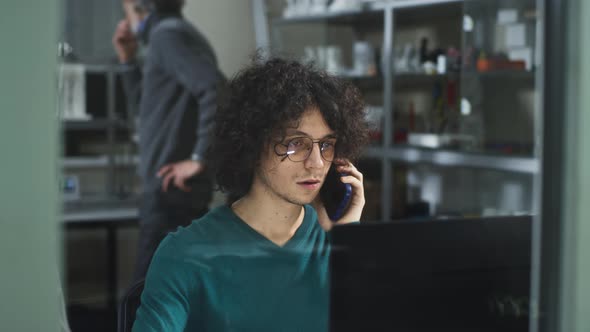 Male Designer Using Computer and Speaking on Cellphone