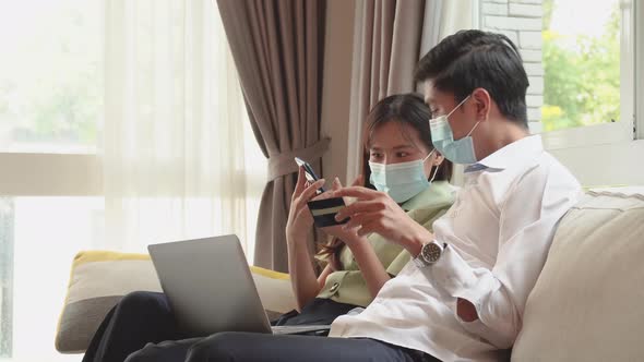 Happy asian couple with medical masks using laptop for ecommerce doing online shopping together 
