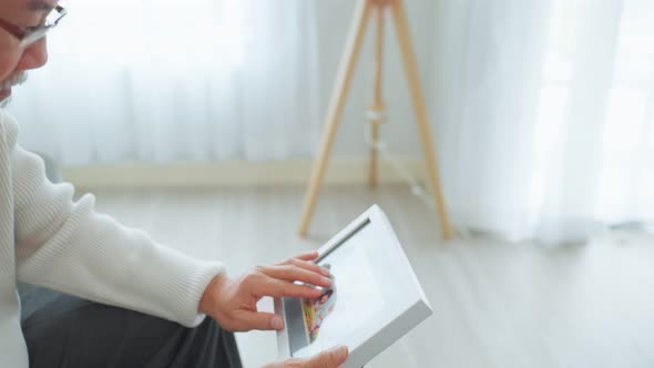 Asian senior male sitting alone on sofa and look at family photographs.