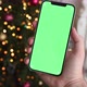 Man holding modern smartphone with green screen chromakey near Christmas tree lights on background - VideoHive Item for Sale
