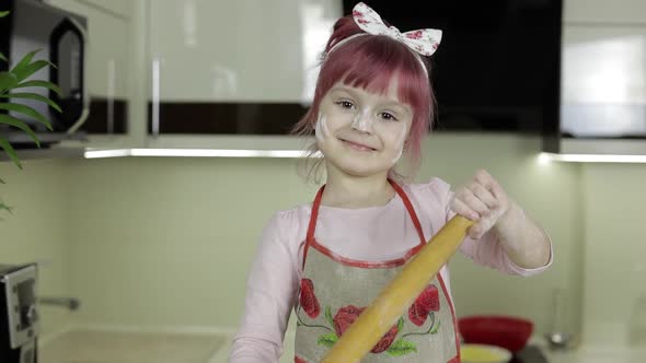 Little Child Girl in the Kitchen Dressed in Apron and Scarf with Rolling Pin