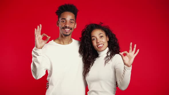 Young African Couple Making OK Sign Over Red Background. Winner. Success