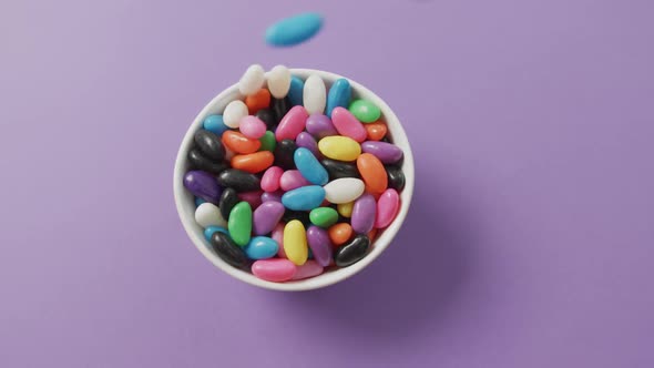 Video of close up of multi coloured sweets falling into bowl over purple background