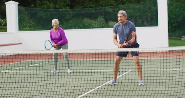 Video of happy biracial senior couple during training on tennis court