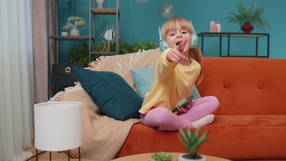 Child Girl Kid with Smartphone in Headphones Dancing Singing Listening Music at Home Alone on Sofa