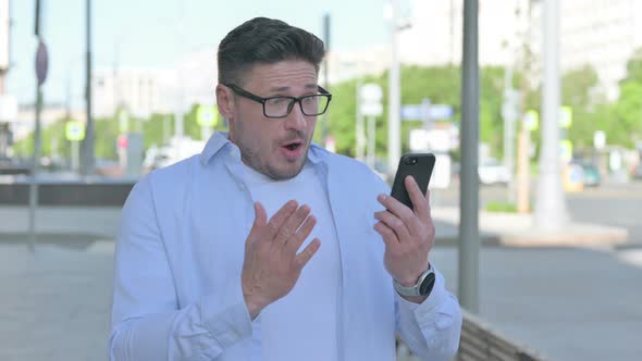 Upset Man Reacting to Loss on Smartphone Outdoor