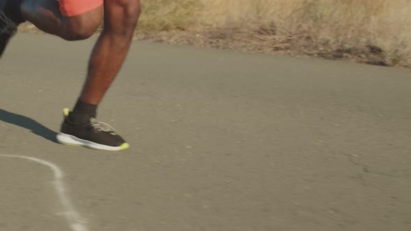 Male black legs run along road in sneakers. Legs run along the road on training, side view, closeup.