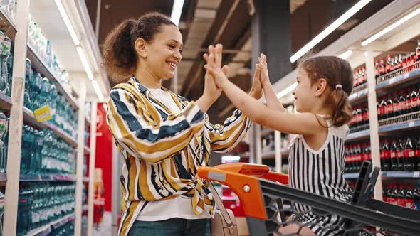 Girl Sits in a Supermarket Trolley and Claps Her Hands on Her Mother's Hands