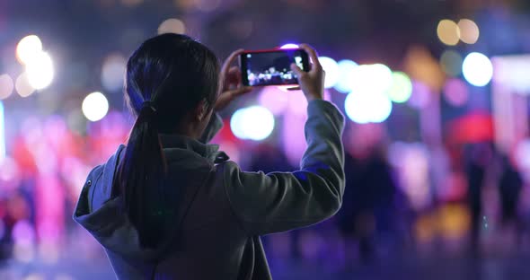 Woman take photo on mobile phone in the street at night