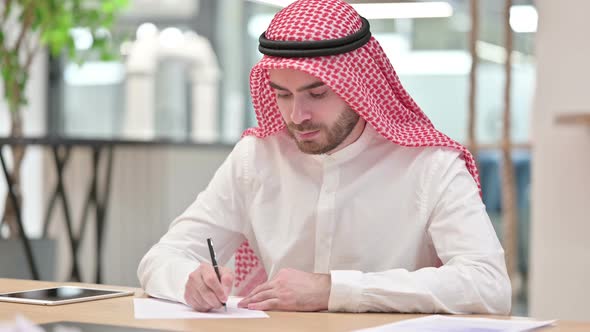 Focused Arab Businessman Writing on Paper in Office 