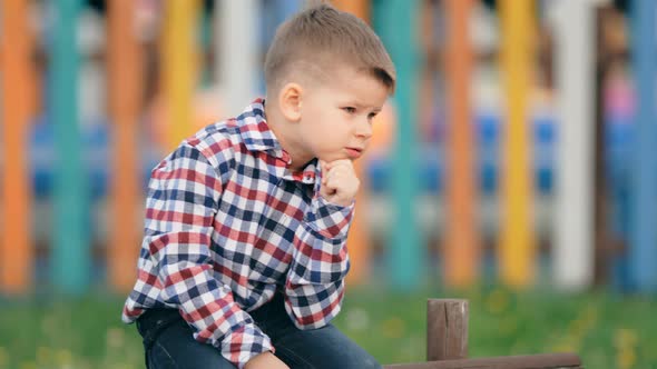 Pensive Little Boy Sitting Outside on a Colourful Background