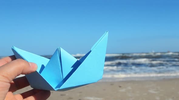 Person Holding Blue Paper Boat in Hand and Plays Floating in Air on Background