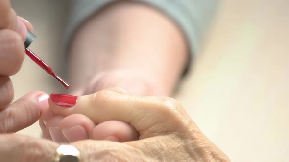 Manicurist Applying Red Varnish To Senior Woman.