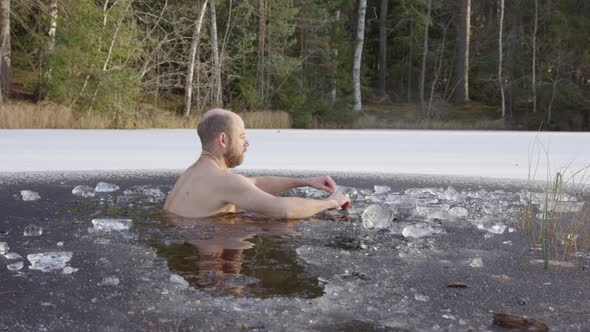 SLOW MOTION - A male ice bather sits down into the icy water to begin