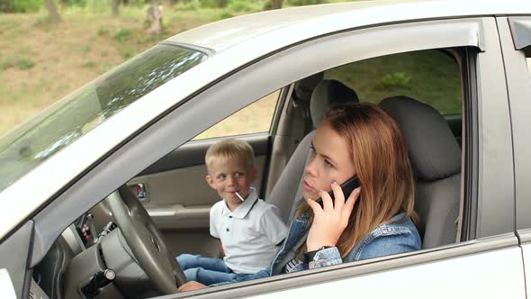 A Child Indulges in a Car Sitting in the Front Seat Mother Talking on the Phone