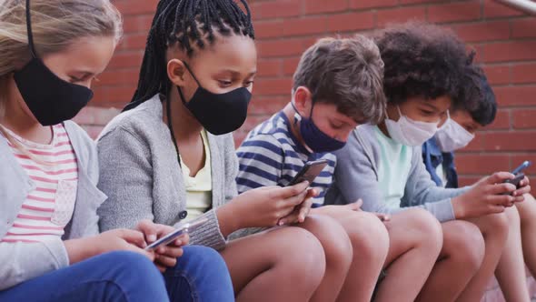 Group of kids wearing face masks using smartphones while sitting together