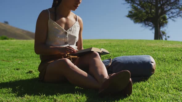 African american woman sitting on grass reading book in park