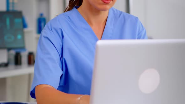 Close Up of Young Medical Assistant Typing at Laptop and Raising Head Smiling