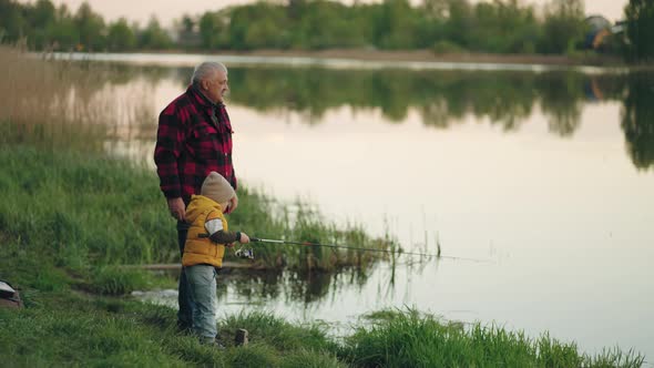 Little Boy is Fishing on Shore of Lake Grandfather is Teaching His Grandson