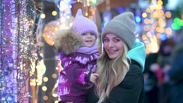 Portrait of Mom and her little daughter are walking at the street Christmas market