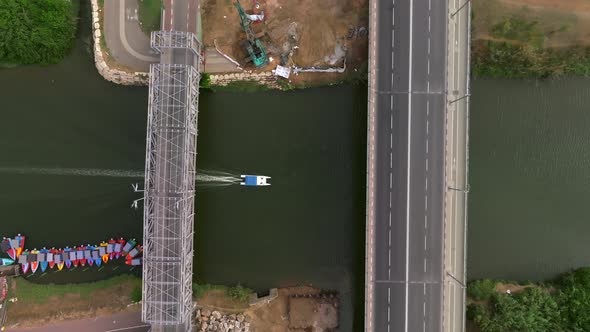 Small White boat heading upstream of the Yarkon river passing under city bridges.