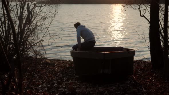 Man Sitting On Boat Near River And Enjoying The Sunset. Man Sitting Among Pond And Looking To Sunset