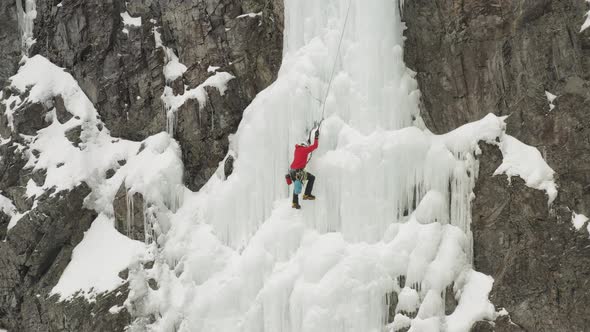 Lone climber advances up frozen cascade spectacular aerial 4K