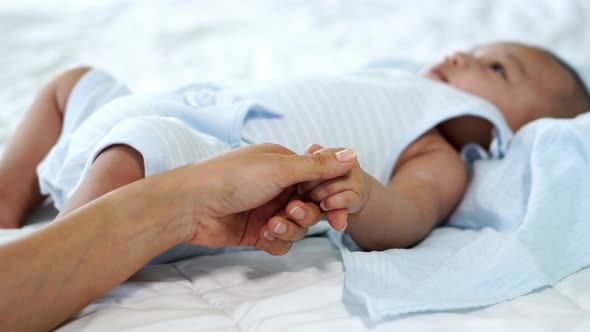 baby hand holding finger of mother on a bed