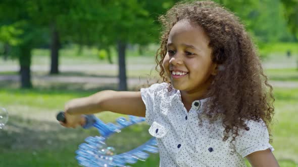 Joyful African Girl Swinging Wand and Making Bubbles alt