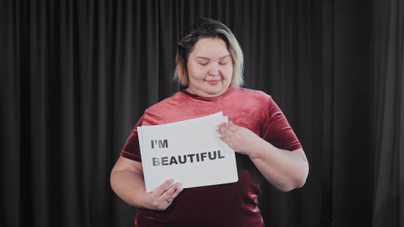 A Confident Flirty Overweight Woman Holding a Nameplate with a Sign I'M BEAUTIFUL and I LOVE MYSELF