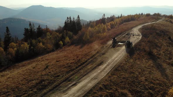 Quad bikes and SUV going on mountaint road. Sunny Autumn daytime. Aerial view.