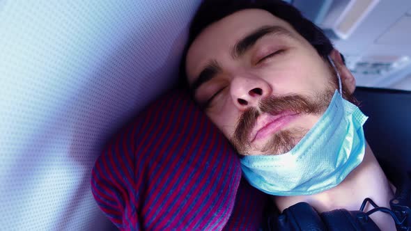 Tired Man is Sleeping in a Plane with Mask Taken Off and Wearing It Back on His Face in Closeup