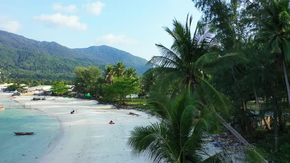 Palms and exotic trees on the sandy beach with tourists. Tranquil tropical lagoon. Thailand