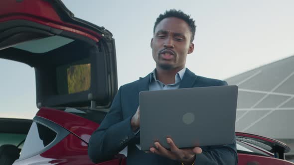 African American Man Holding Wireless Laptop While Leaning on His Luxury Red Car